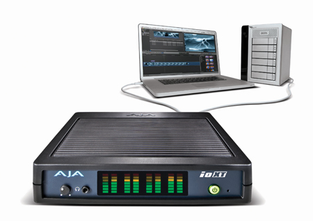 A black AJA ioXT video interface connected via cable to a laptop and a silver external storage device.