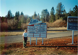 A person stands beside a large white directory sign for the Litton Building in front of a treeline.