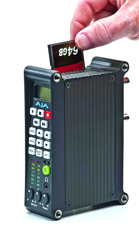 A hand inserts a 64GB memory card into the top slot of a black handheld electronic device.