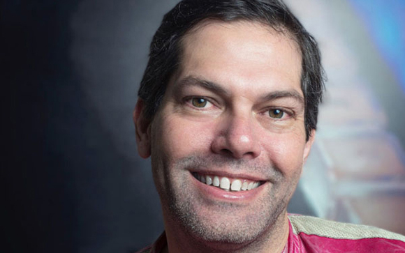 A close-up portrait of a man with dark hair and a slight smile.