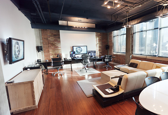 A modern office featuring a lounge with cream sofas, wooden floors, and desks with computer monitors.