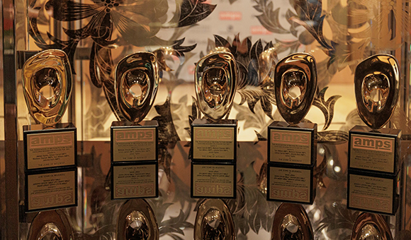 Five gold trophies with black bases arranged in a row against a floral patterned glass background.