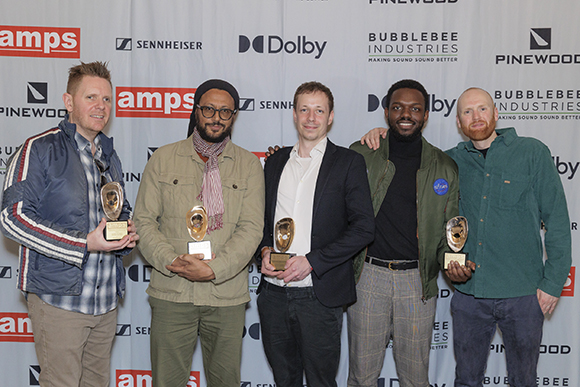 Five men posing together while holding gold awards in front of a white backdrop with various brand logos.