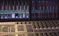 A close-up view of a professional audio mixing board with glowing red and blue lights and vertical sliders.