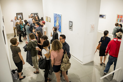 A group of people standing in a white-walled art gallery viewing various framed artworks.