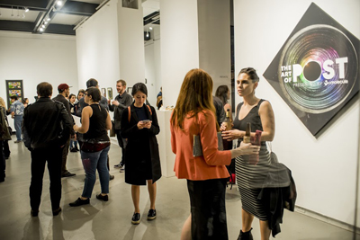 People standing and talking in a bright art gallery near a large black circular poster.