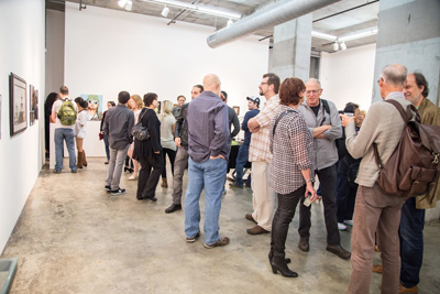 A group of people standing in a bright art gallery looking at paintings on white walls.