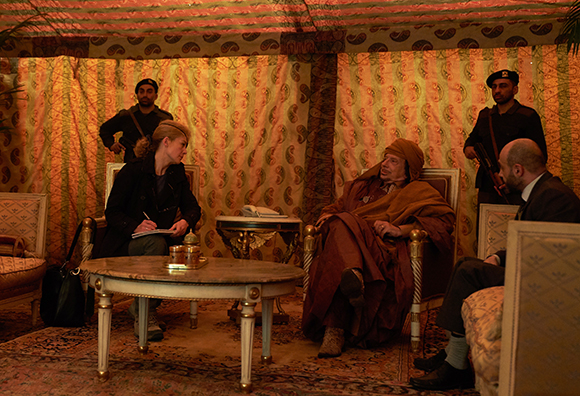 Four people sit in chairs around a small table in a room with patterned fabric walls.