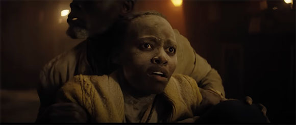 A young girl with a fearful expression is held closely by a man in a dimly lit setting.