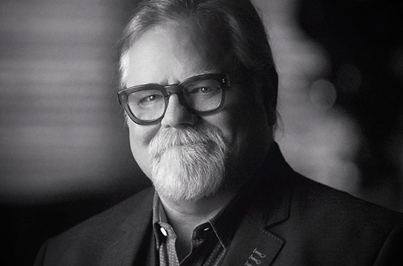 Black and white portrait of a man with glasses and a full white beard wearing a suit jacket.