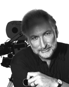 Black and white portrait of a man with a beard leaning near a professional film camera.