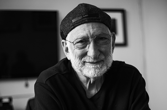 Black and white close-up portrait of an elderly man with a white beard, wearing glasses and a dark cap.