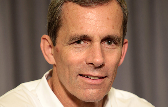 Close-up portrait of a middle-aged man with short brown hair and a white shirt.
