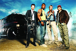 Four men posing outdoors in front of a black SUV under a blue sky.