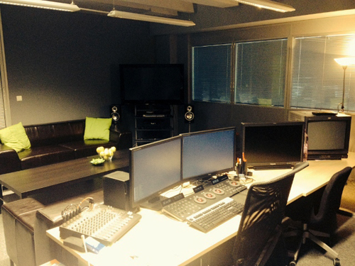 A lounge with a black leather sofa and a desk with multiple computer monitors and control panels.