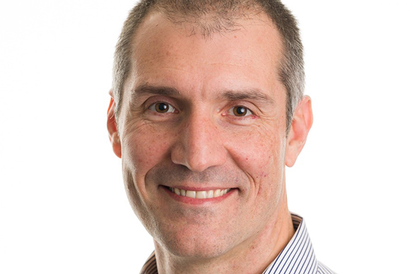 A close-up portrait of a middle-aged man with short brown hair smiling against a white background.