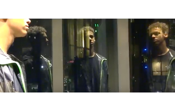 A man in profile looks at his reflection in a dark window pane.