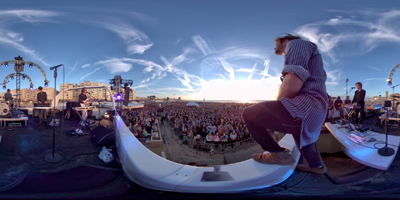 Panoramic view from a stage overlooking a large crowd gathered outdoors during a sunset.