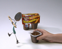 A spoon character stands next to a Spoonnibbles snack pack box and a hand holding a small pudding cup.