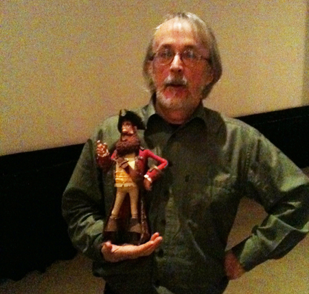 A man with glasses and a beard holding a small pirate figurine in front of his chest.