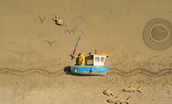 A miniature blue and yellow boat on sand with a fishing line catching a small, star-shaped object.