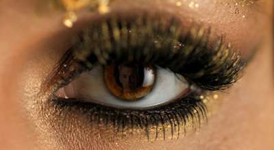 Extreme close-up of a human eye with long lashes and gold glitter eyeshadow.