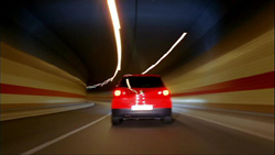 A red car driving through a tunnel with motion blur and light streaks on the ceiling.