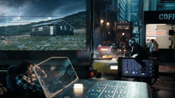 A person uses a transparent laptop in a dark city environment near a large screen showing a landscape.