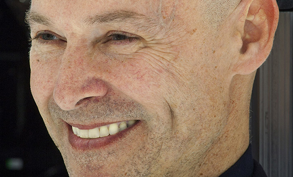 Close-up profile of a middle-aged man smiling with visible wrinkles and freckles.