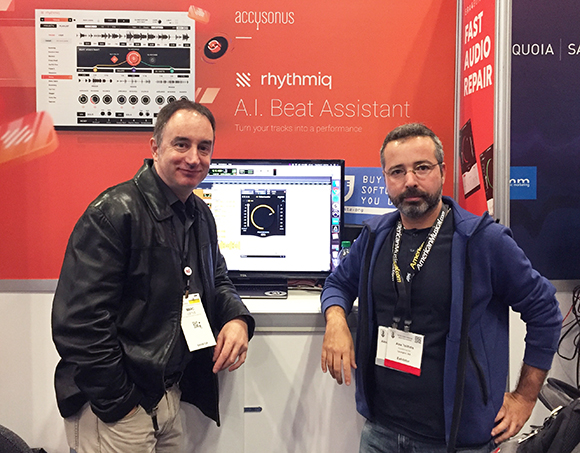 Two men stand in front of a booth with music production software displayed on a screen and a banner that reads "accysonus rhy