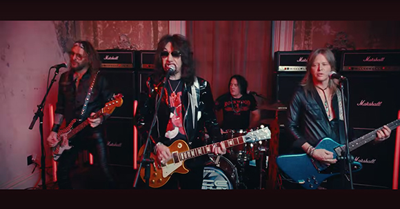 Four band members performing with electric guitars and drums in front of large Marshall amplifiers.