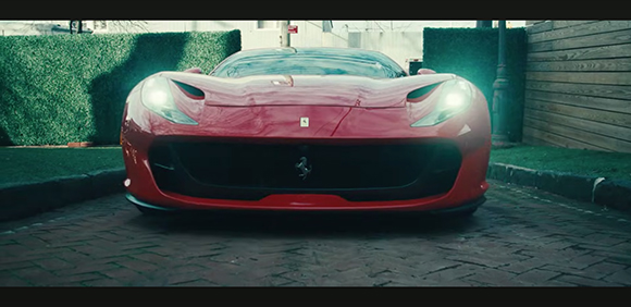 Front view of a red Ferrari sports car parked on a brick driveway in front of a green hedge.