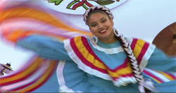 A smiling woman in a blue and multi-colored traditional dress dancing with flowing fabric.