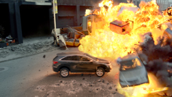 A large orange and yellow explosion erupting amidst several cars on a paved street.