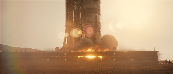 A large rocket ignites on a launch platform amidst bright orange flames and thick smoke at sunset.