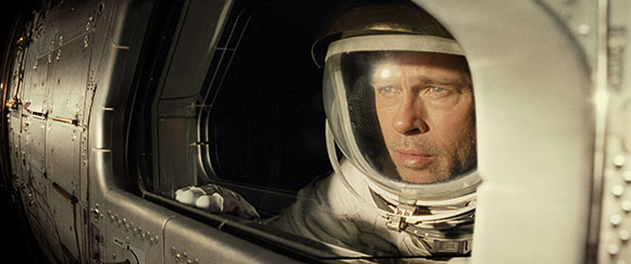A man in a white astronaut suit looks out of a small, circular spacecraft window into the darkness.