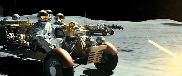 Astronauts in white spacesuits driving lunar rovers across a desolate, cratered moon landscape.