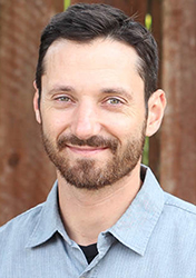 A man with short dark hair and a beard smiling at the camera.