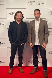 Two men standing on a red carpet in front of a white Tribeca Festival 2021 backdrop.