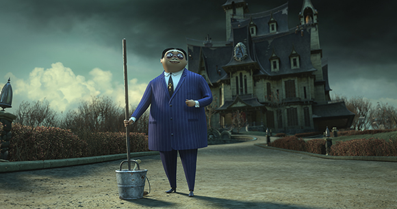 A large man in a blue pinstripe suit holds a mop next to a bucket in front of a large, dark mansion.