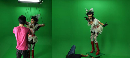 A person in a white costume and red boots stands against a green screen, held by thin wires.