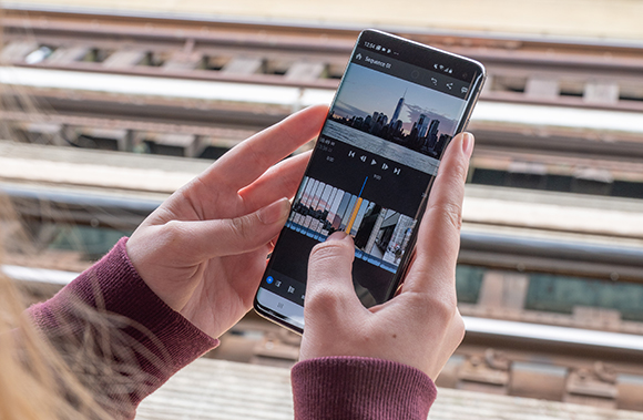 Hands holding a smartphone showing a video editing timeline with a cityscape video clip.