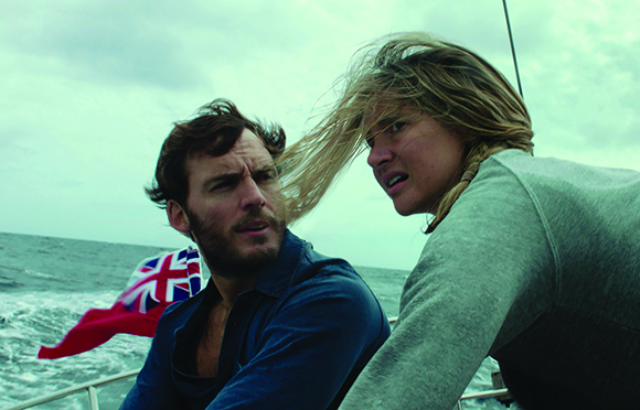 A man and a woman with windblown hair look intensely toward the side while on a boat in the ocean.