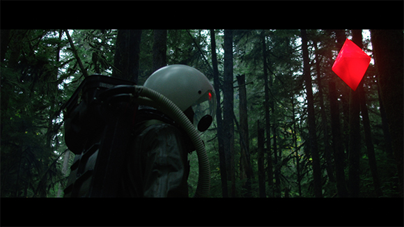 An astronaut in a white helmet stands in a dark forest looking at a floating, glowing red diamond.