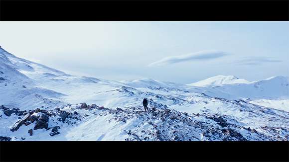 A person walking across a vast, snow-covered mountain range under a pale sky.
