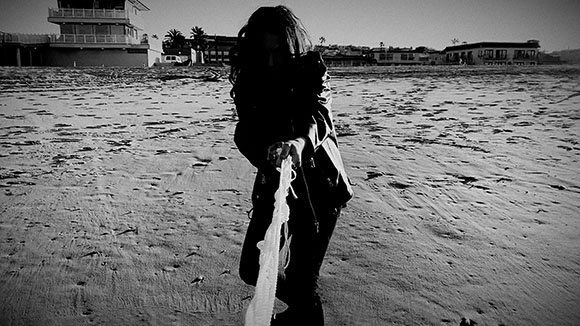 Silhouette of a person on a sandy beach holding a long piece of white fabric.