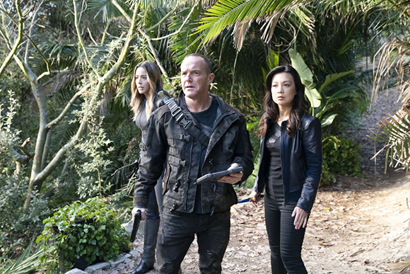 Three people in dark clothing walk through a lush, tropical forest setting.
