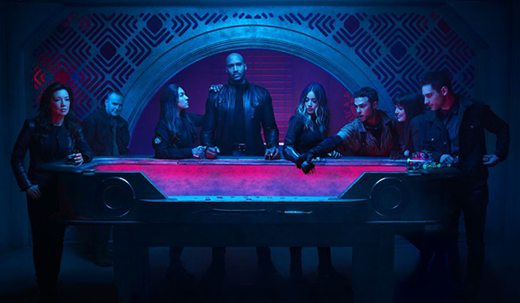 A group of people in dark clothing stand around a large, glowing red table in a blue-lit room.
