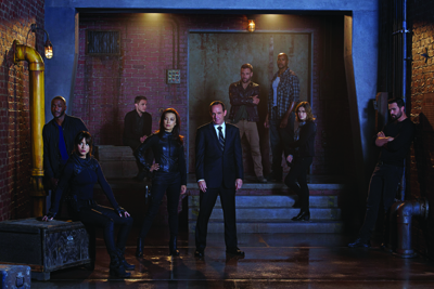 A group of diverse people in dark clothing posing in a dimly lit industrial room with brick walls.
