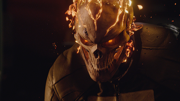 A close-up of a figure with a skull-shaped head engulfed in glowing orange flames.